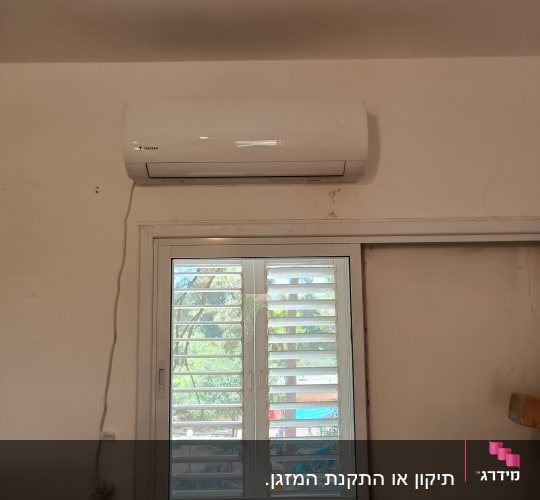 מזגן מותקן מעל חלון עם תריסים